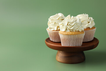 Tasty vanilla cupcakes with cream on green background, space for text
