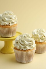 Tasty vanilla cupcakes with cream on pale yellow background, closeup