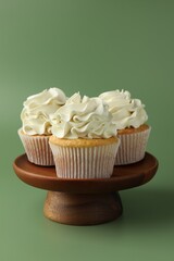 Tasty vanilla cupcakes with cream on green background