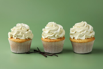 Tasty cupcakes with cream and vanilla pods on green background