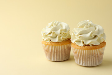 Tasty vanilla cupcakes with cream on pale yellow background, space for text