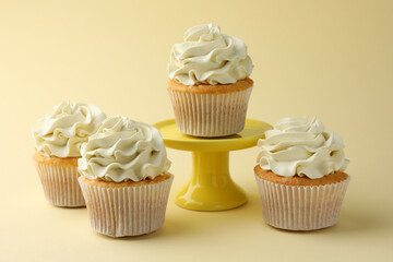 Tasty vanilla cupcakes with cream on pale yellow background, closeup