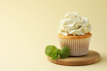 Tasty vanilla cupcake with cream and mint on pale yellow background, space for text