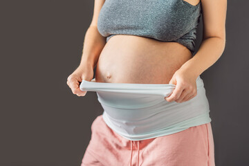 Pregnant bliss: Mom-to-be embraces her baby bump with a soft fabric bandage, providing gentle...