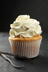 Tasty cupcake with cream and vanilla pods on black table, closeup