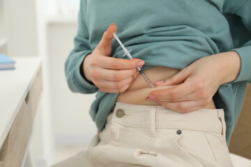 Diabetes. Woman making insulin injection into her belly indoors, closeup