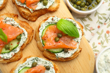Tasty canapes with salmon, capers, cucumber and sauce on table, top view