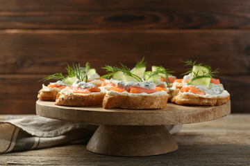 Tasty canapes with salmon, cucumber, cream cheese and dill on wooden table