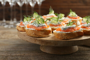 Tasty canapes with salmon, cucumber, cream cheese and dill on wooden table, closeup