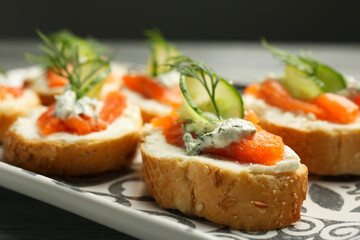 Tasty canapes with salmon, cucumber, cream cheese and dill on table, closeup