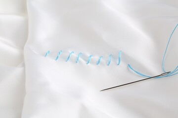 Sewing needle with thread and stitches on white cloth, top view
