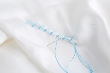 Sewing needle with thread and stitches on white cloth, closeup
