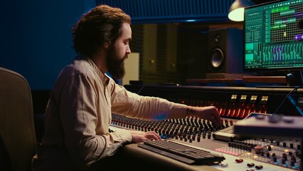 Mixing engineer focuses on blending and balancing individual tunes of a recording to create song, audio editing software in control room. Expert deals with technical aspects of sound. Camera B.