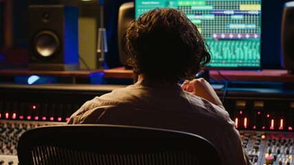 Skilled sound designer enjoying his own music creating at mixing console in control room, feeling...