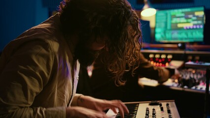 Singer performer creating a song on piano midi controller in studio, recording notes on electronic...