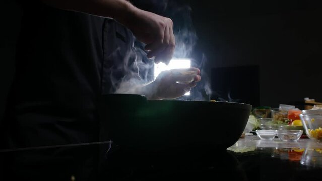 Chef of the cooking show adds a variety of spices to the food he prepares in a large frying pan. Mid shot. 4k.