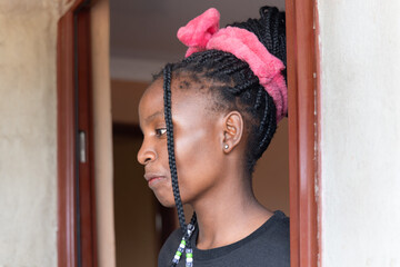 african village , african teenager girl with braids standing in front of the door of the house