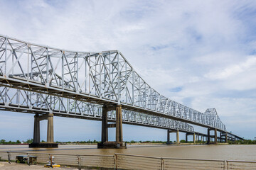 Obraz premium The Crescent City Connection bridge over the Mississippi River with lush green trees, plant and grass, blue sky and clouds in New Orleans Louisiana USA