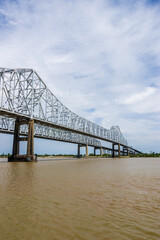 The Crescent City Connection bridge over the Mississippi River with lush green trees, plant and grass, blue sky and clouds in New Orleans Louisiana USA