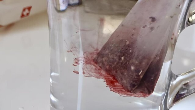 Mesmerizing infusion of a tea bag in clear glass, dynamic diffusion of red herbal flavors