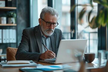 Fototapeta premium Confident serious mature businessman using laptop computer, taking notes, working project in modern office. 60 years old female, financier working with documents at workplace. Successful business