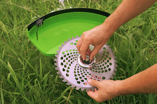 Installing a saw blade on a new green brush cutter. Gardener sets up a saw blade against a grassy field, close up. Preparing the brush cutter for work. Servicing garden tools.