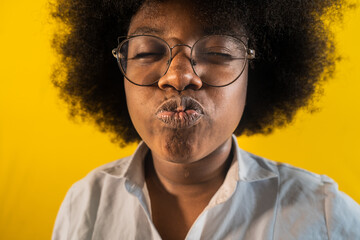 mujer afrolatina en un fondo de color amarillo mientras usa lentes y tira besos 