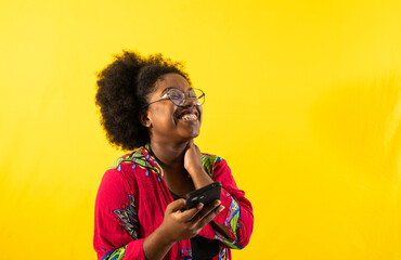 mujer joven afrolatina sonriendo y usando lentes mientras sostiene su movil y esta en un fondo de...