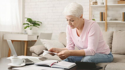 Elderly Woman Reviewing Financial Documents at Home in Daylight