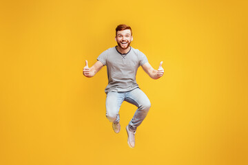 Happy joyful man jumping up in air, demonstrating thumbs up