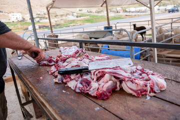 The butcher cuts the meat with knife on wooden cutting board.Close-up piece of raw meat with a chef's knife outdoors in springfield with sheeps barn  in the background - obrazy, fototapety, plakaty
