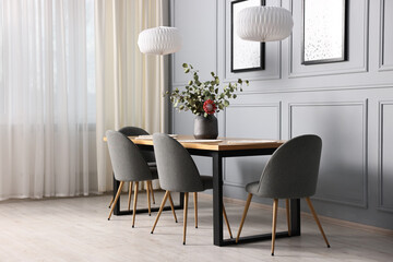Soft chairs, table and vase with plants in stylish dining room