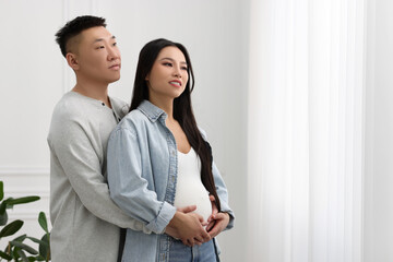 Man touching his pregnant wife's belly at home, space for text