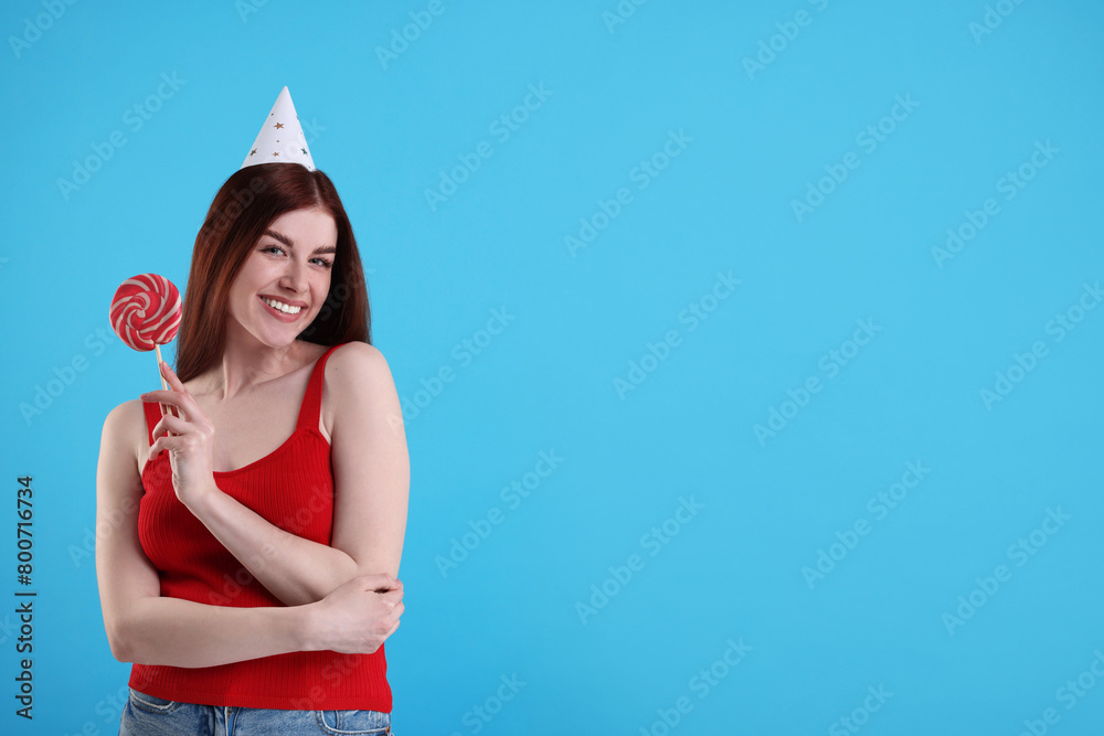 Canvas Prints Happy woman in party hat with lollipop on light blue background, space for text