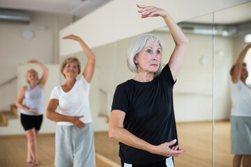 Active mature woman visiting choreography class with group of aged females, learning classical...