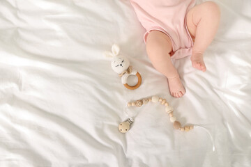 Cute baby with rattle and teether toys on sheets, top view. Space for text