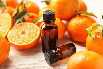Bottles of tangerine essential oil and fresh fruits on wooden table, closeup