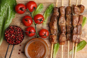 Tasty cooked marinated meat served with sauce and tomatoes on wooden table, flat lay