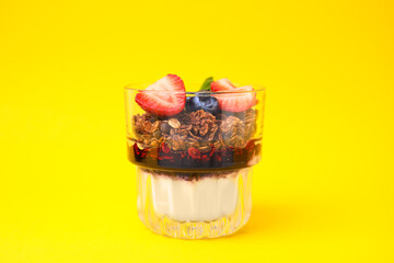 Tasty granola with berries, jam and yogurt in glass on yellow background