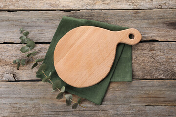 Cutting board, eucalyptus branch and napkin on wooden table, top view