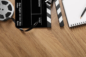 Movie clapper, film reel, notebook and pen on wooden table, flat lay. Space for text