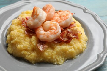 Plate with fresh tasty shrimps, bacon and grits on light blue wooden table, closeup