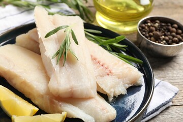 Pieces of raw cod fish, rosemary and lemon on wooden table, closeup