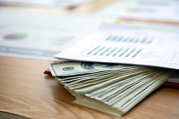 On office desk, stack of US dollars is accompanied by financial charts and graphs, illustrating...
