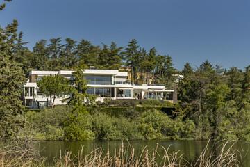 a beautiful modern style mansion house surrounded by trees on the shore of a lake