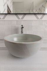 Bathroom with a half-circumference single-bowl sink in baked terracotta, not embedded in a marble countertop, decorative paper on the wall and a mirror with a black metal edge