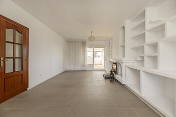 A large empty living room with built-in shelves and a fireplace with grills and crystal chandeliers...