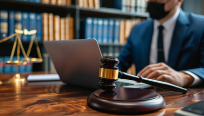 A man in a suit is sitting at a desk with a laptop and a gavel