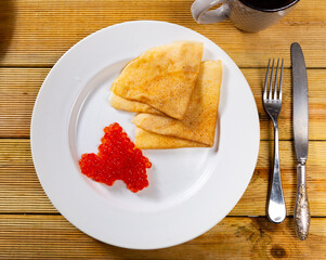 Pancakes with red caviar dished up in flat service plate. Traditional Russian cuisine