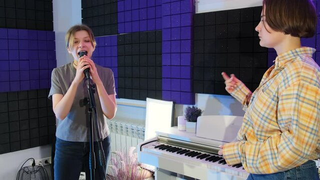 Young woman singer takes singing lessons from qualified vocal coach in studio. Female teacher snaps fingers creating right rhythm slow motion
